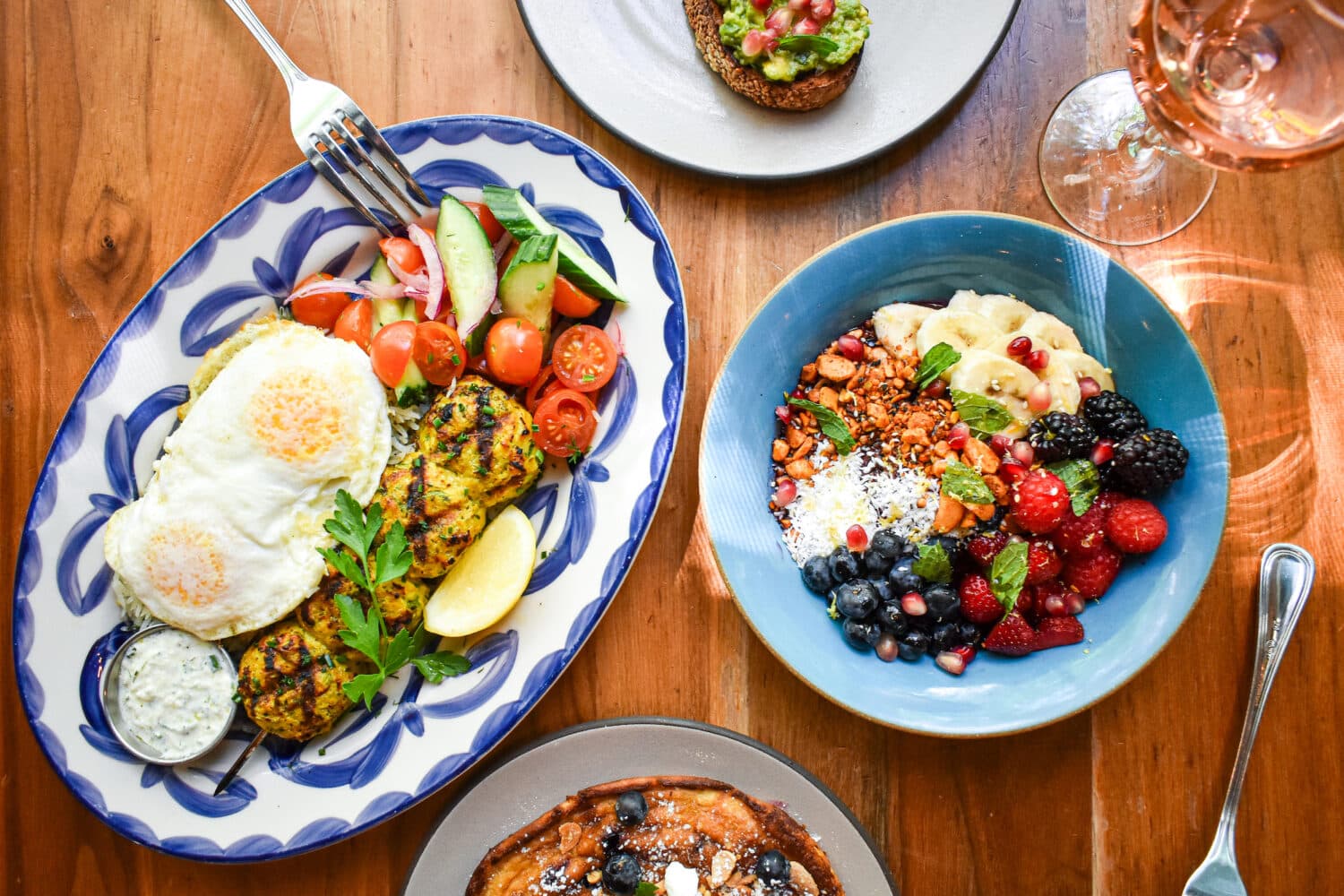 over head photo looking down at a variety of Ema brunch dishes including avocado toast, eggs and a fruit bowl