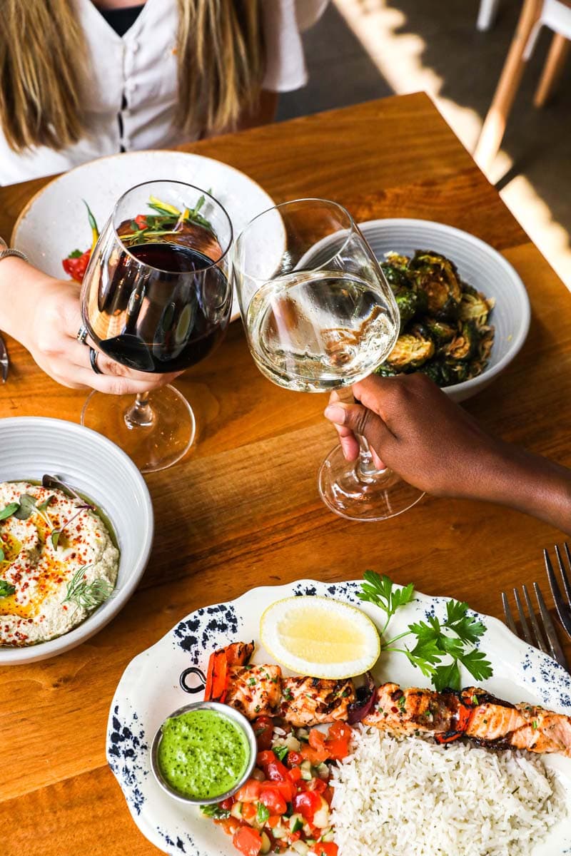 two glasses of wine toasting over a table with a variety of dishes